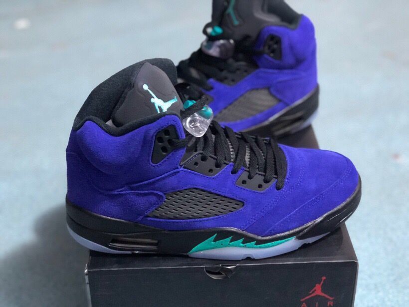 Side and three-quarter view of the purple high-top sneakers with black laces, mesh panels, and a Jordan-branded box in the background.