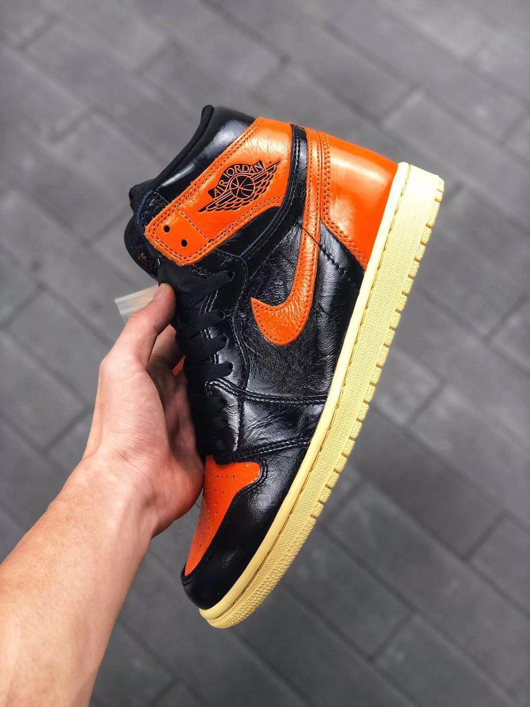Handheld side view showing the orange heel and collar panels, black upper, orange Swoosh, and cream-colored outsole.