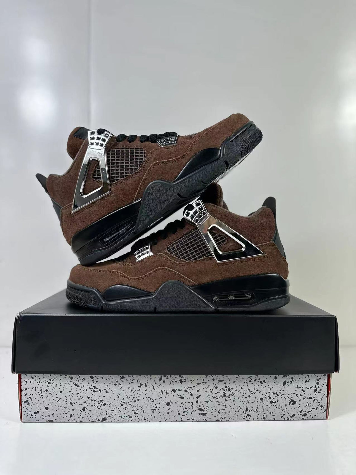 Pair of brown and black sneakers arranged on a black shoe box, showing their side panels and soles.