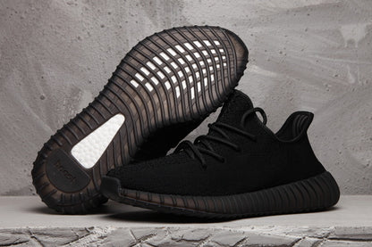 Black Yeezy 350 V2 sneakers shown from the side with the sole of one shoe facing upward.