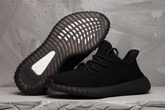 Black Yeezy 350 V2 sneakers shown from the side with the sole of one shoe facing upward.