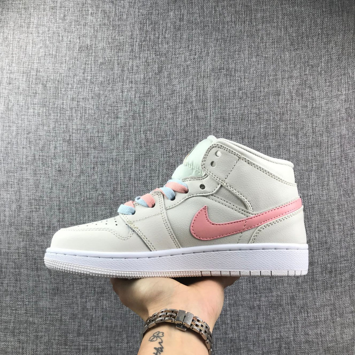 Side profile showing an off-white high-top sneaker with a pastel pink Swoosh and pink-and-blue laces.