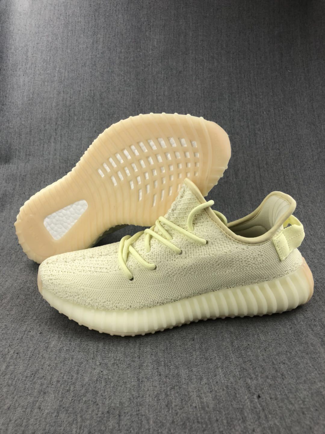 Pale cream 350 V2 sneaker shown beside its translucent ribbed sole for an outsole view.