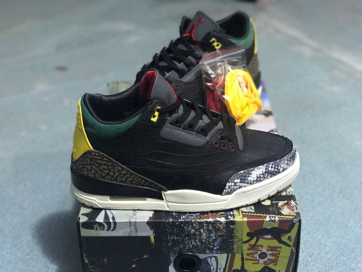 Side view of a black sneaker with green and yellow heel accents, patterned overlays, and a light-colored midsole.