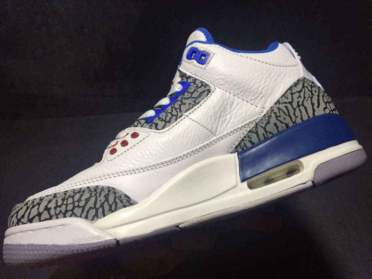 Close side view showing the white upper, blue accents, elephant-print heel and toe panels, and layered sole.