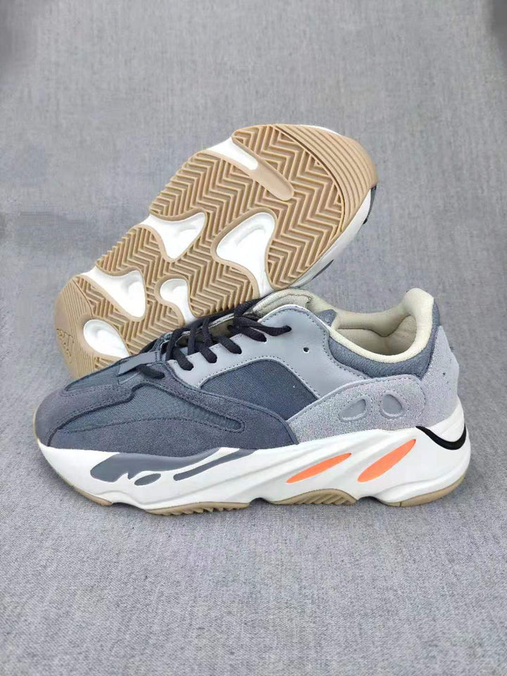 Side view of grey low-top sneakers with black laces, white midsoles, orange accents, and gum-colored outsoles.