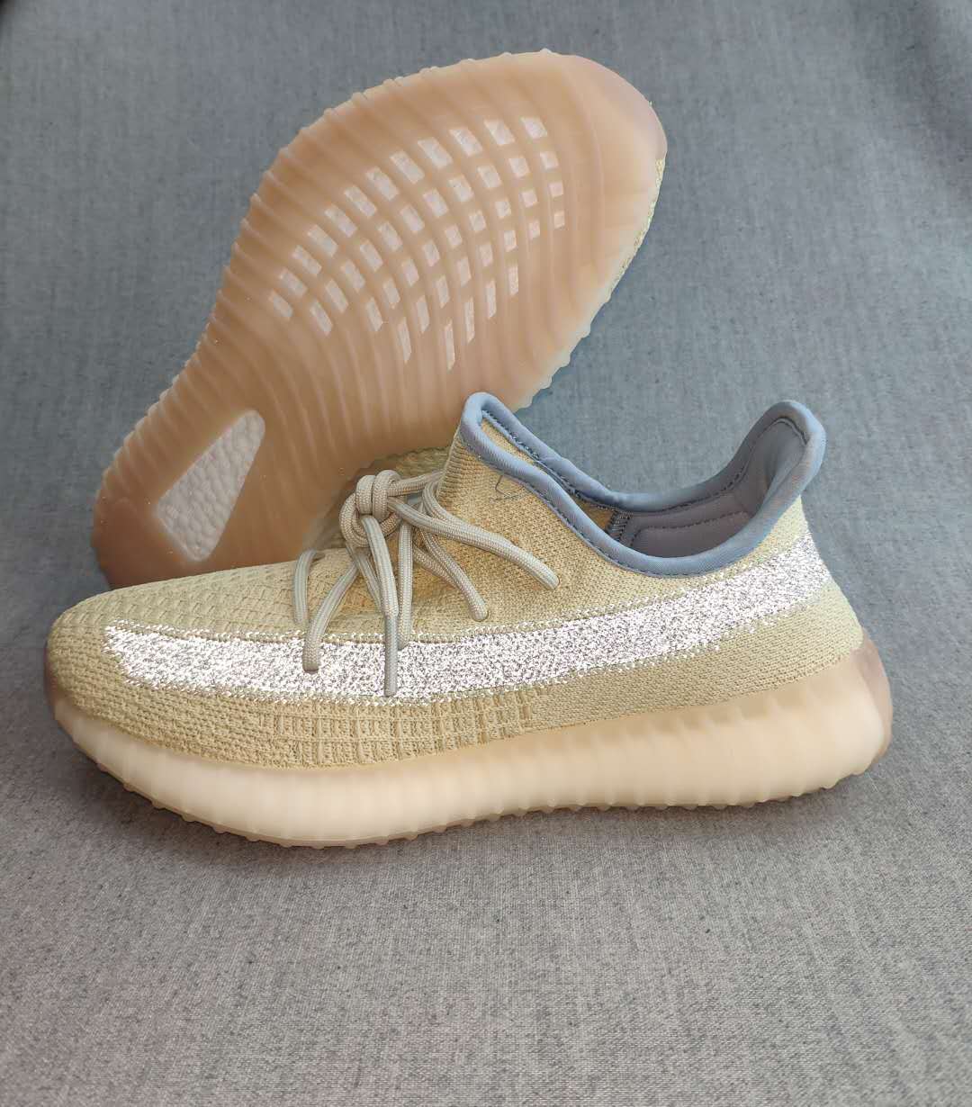 Side view of a beige sneaker with a reflective stripe and translucent ribbed outsole.