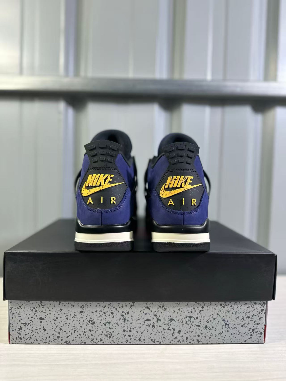 Rear view of a pair of Jordan Air Jordan 4 sneakers showing yellow heel branding and black-and-cream midsole details.