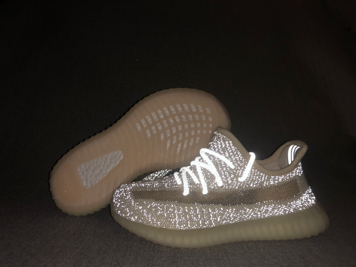 Flash-lit view of the sneakers emphasizing the reflective-looking cream-white upper and translucent sole.