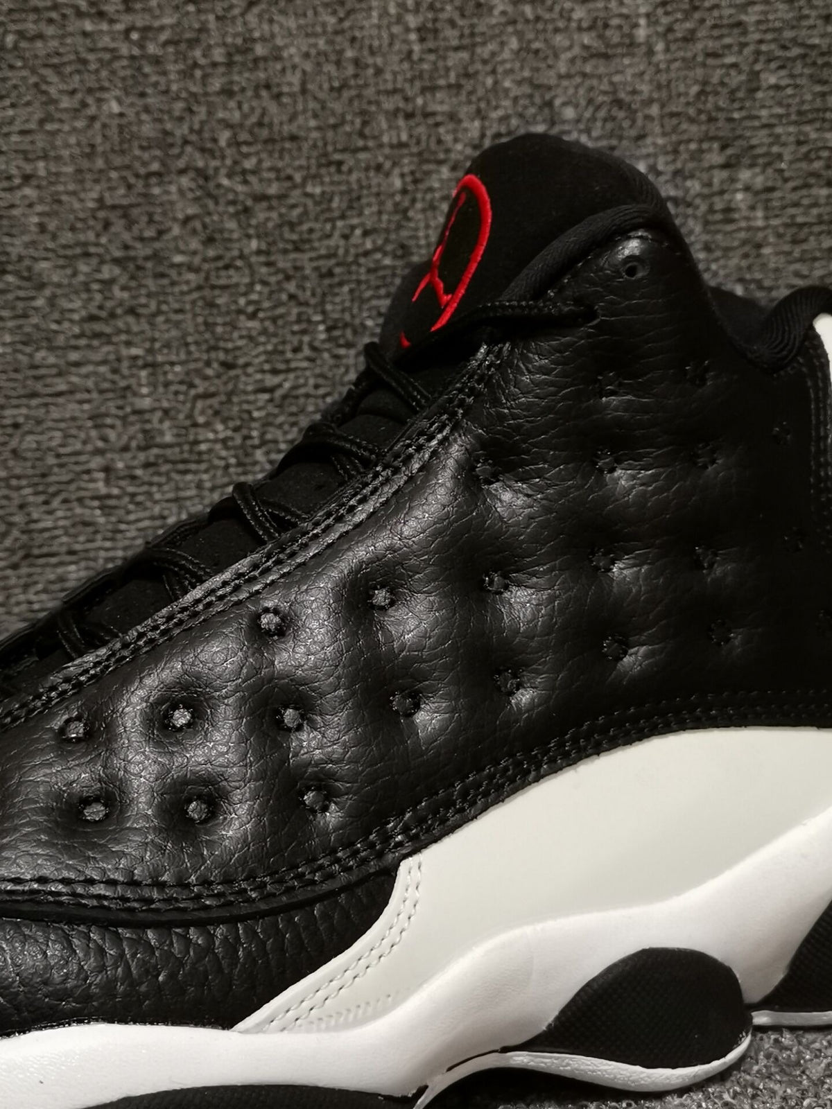 Close-up of the black textured upper, stitching, and red tongue accent