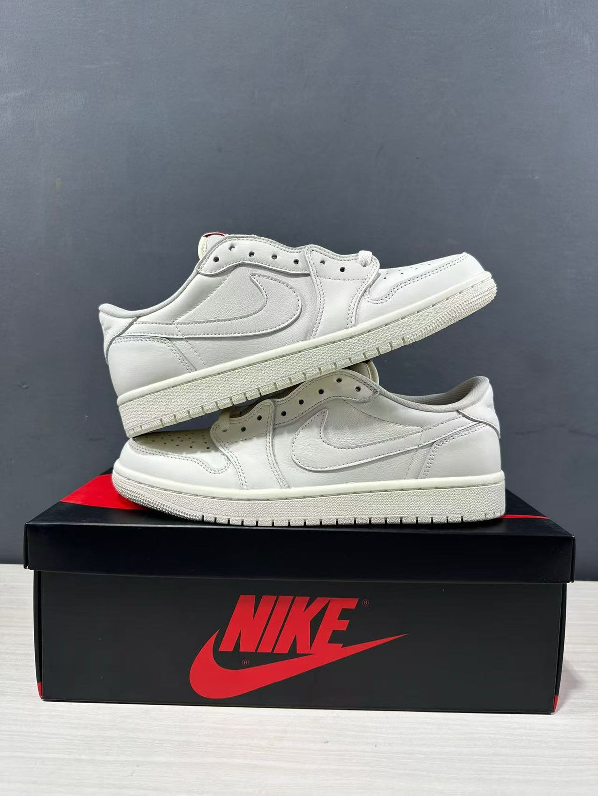 Two white low-top Jordan sneakers stacked on a shoe box, showing the side panels, perforated toe boxes, and rubber outsoles.