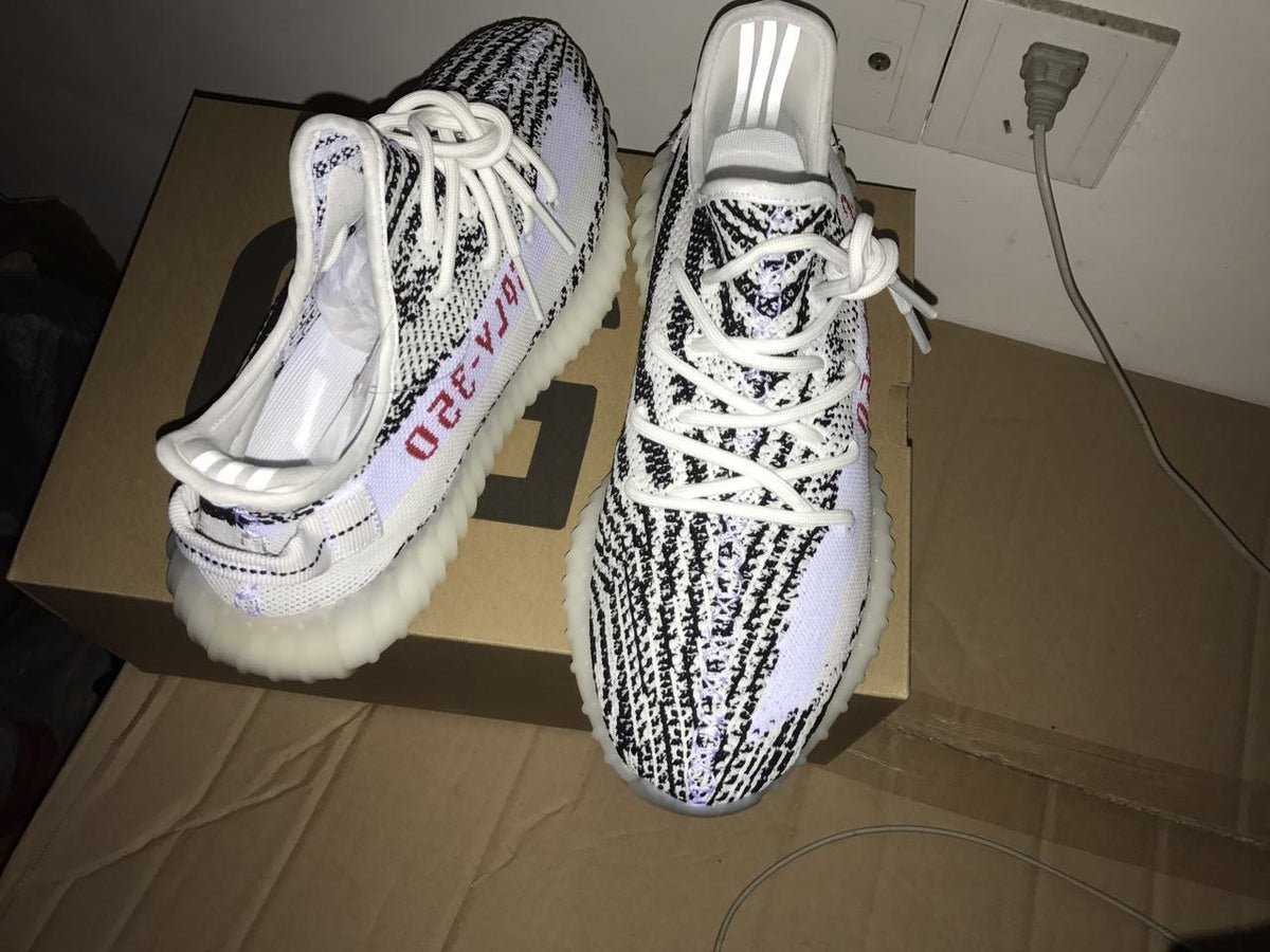 Front and rear views of the sneakers on a box, showing the patterned knit upper and side lettering.