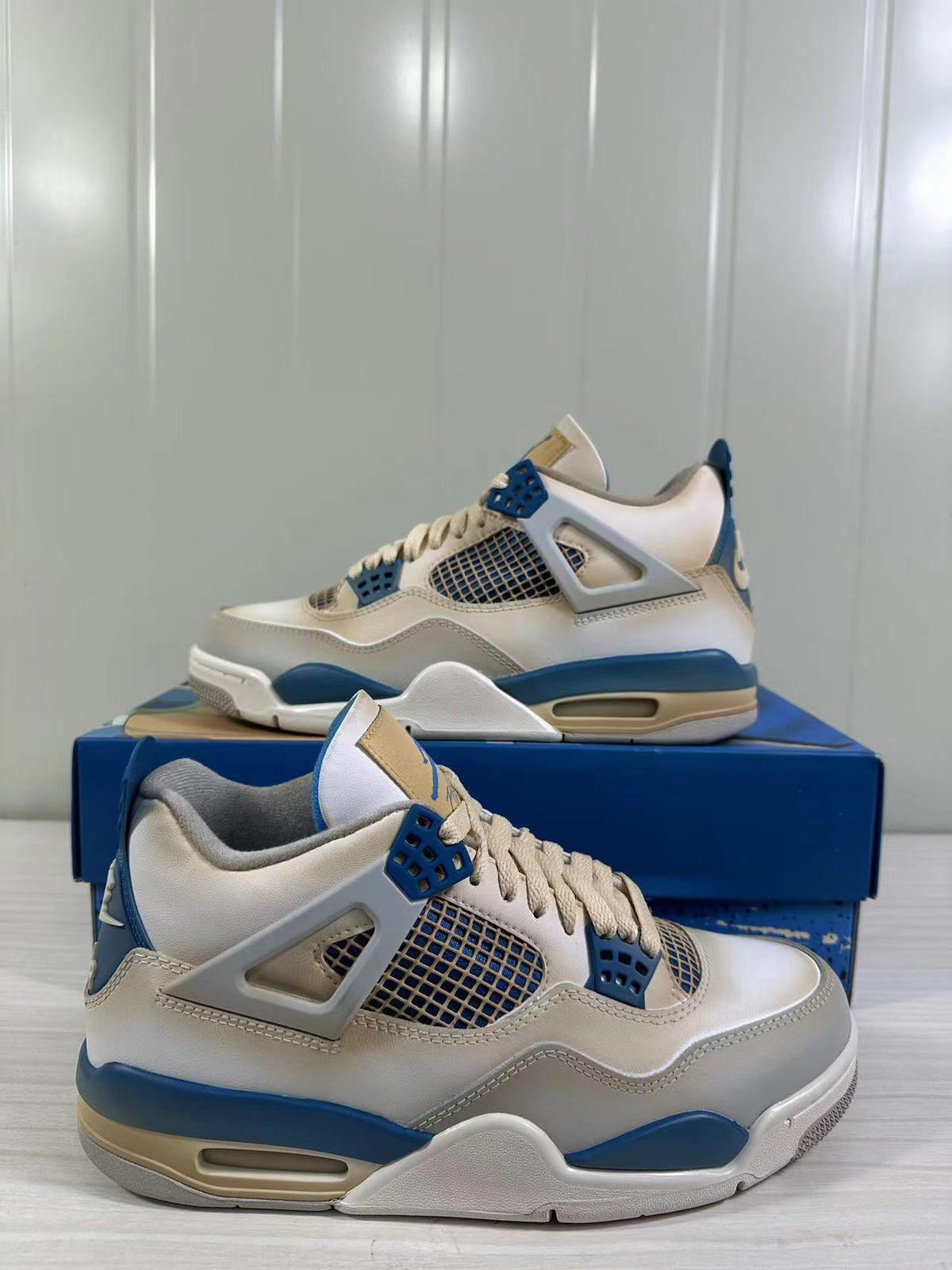 Pair of white and blue Jordan Air Jordan 4 Retro sneakers shown from the side on a blue shoebox.