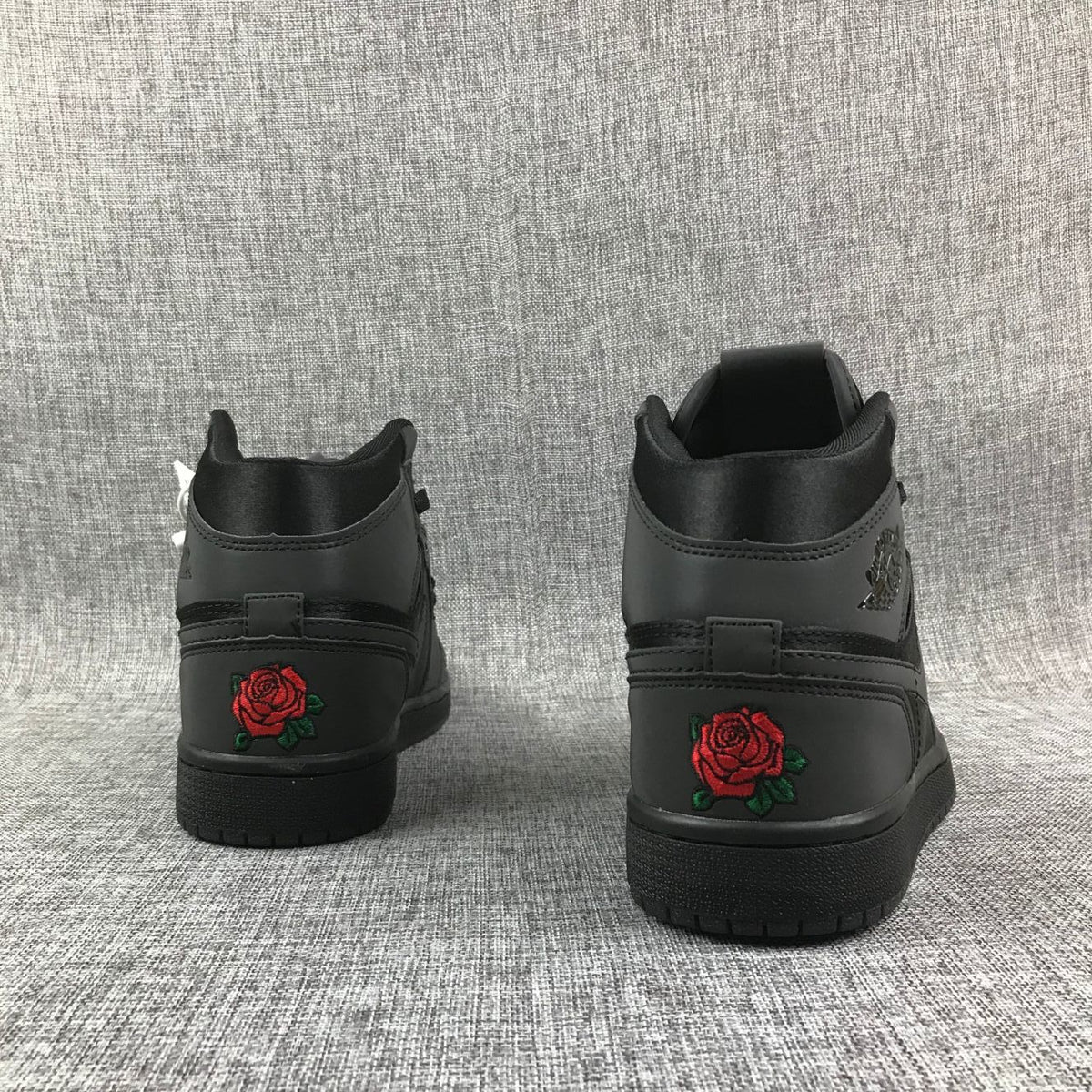 Rear view of the black high-top sneakers showing red rose embroidery with green leaves on the heels.
