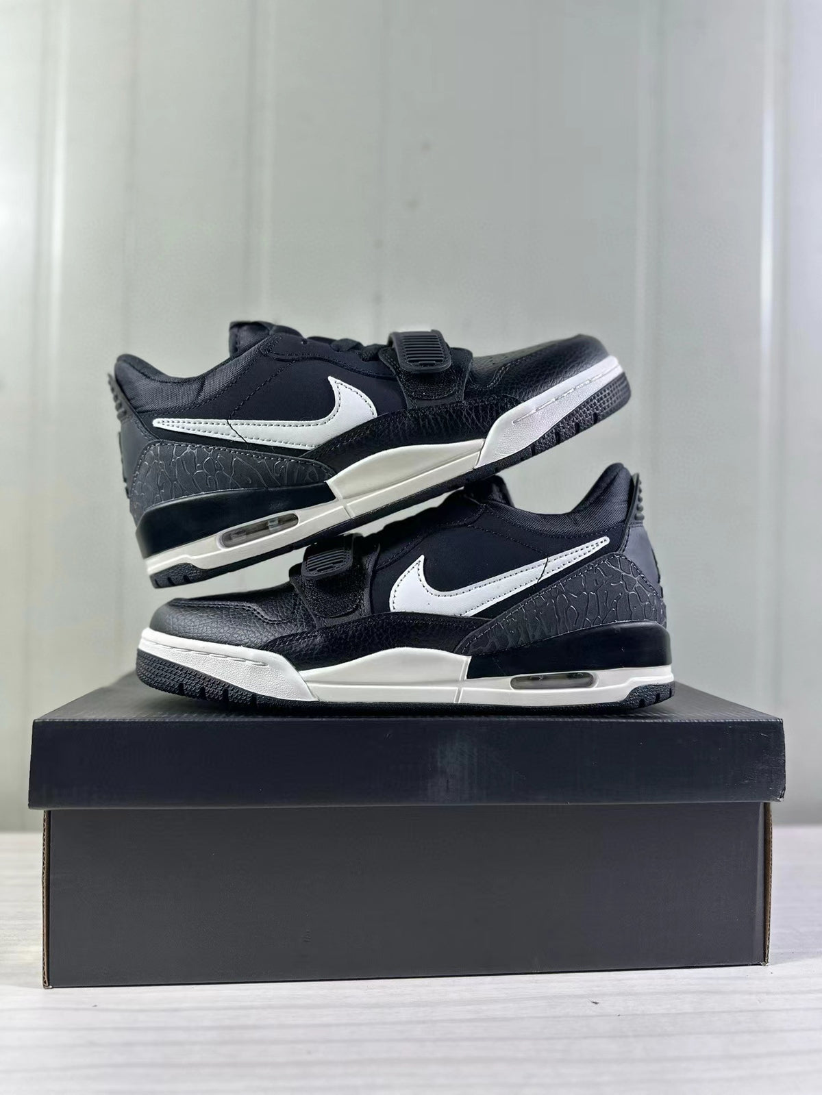 Pair of black and white low-top sneakers showing the side panels, forefoot straps, textured heel sections, and midsole windows.