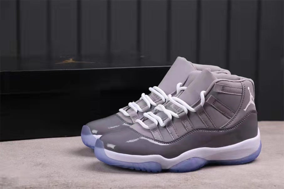 Pair of grey Jordan 11 high-top sneakers shown from a front three-quarter angle with white laces and translucent blue outsoles.
