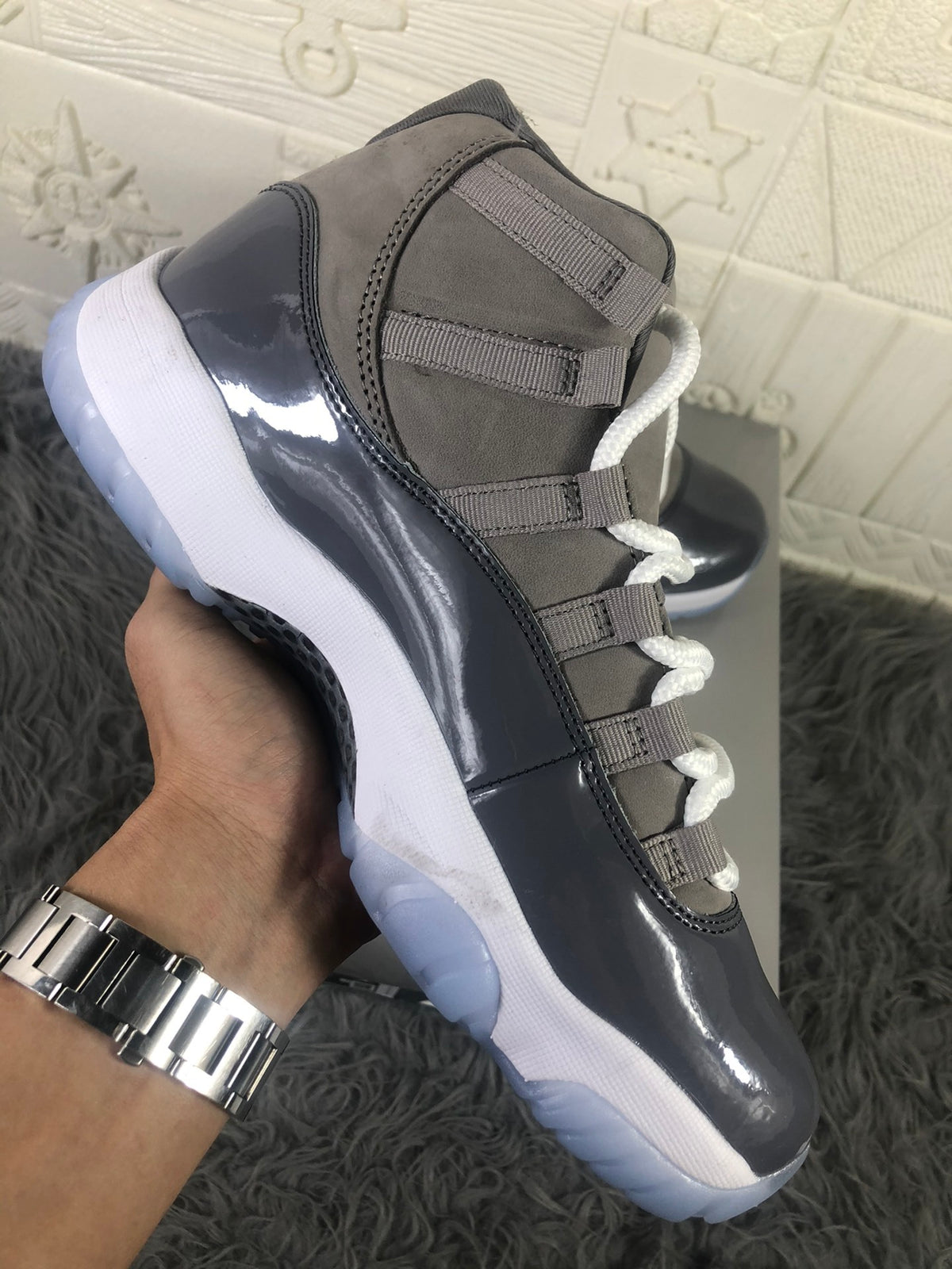 Side view highlighting the grey upper, glossy dark overlay, white midsole, and translucent outsole.