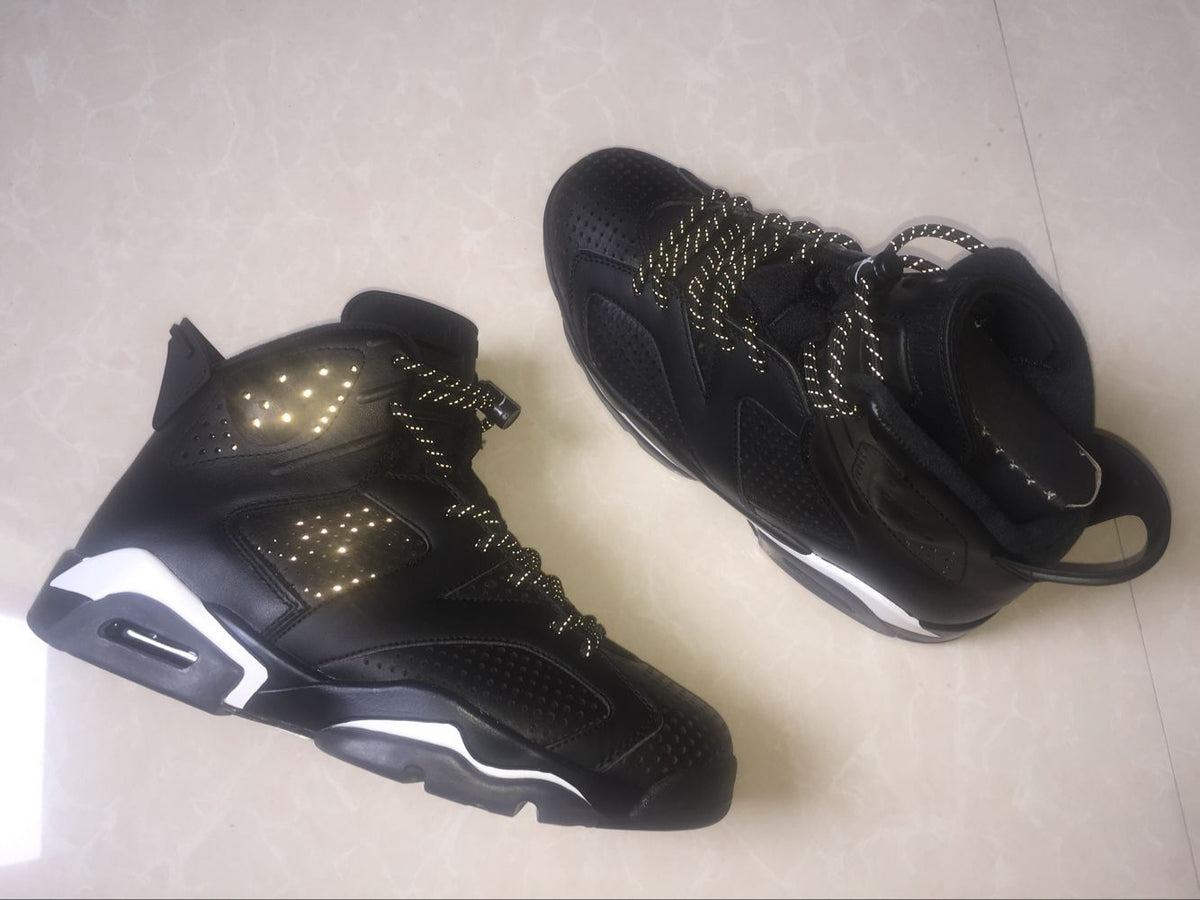 Angled view of two black high-top sneakers showing the perforated upper, reflective-style laces, and white midsole details.