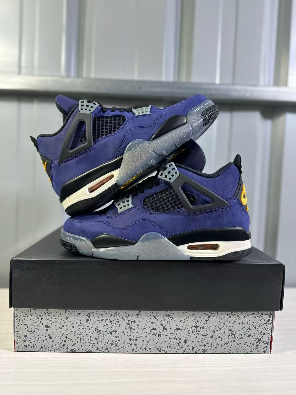 Pair of purple Jordan Air Jordan 4 sneakers arranged on a black shoebox in a side view.