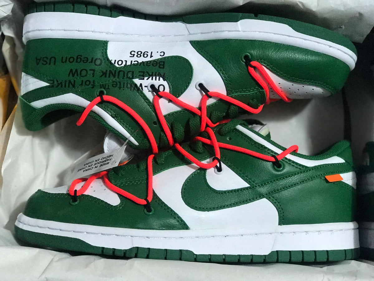 Pair of white and green low-top sneakers with bright red cord-style laces shown in a box.