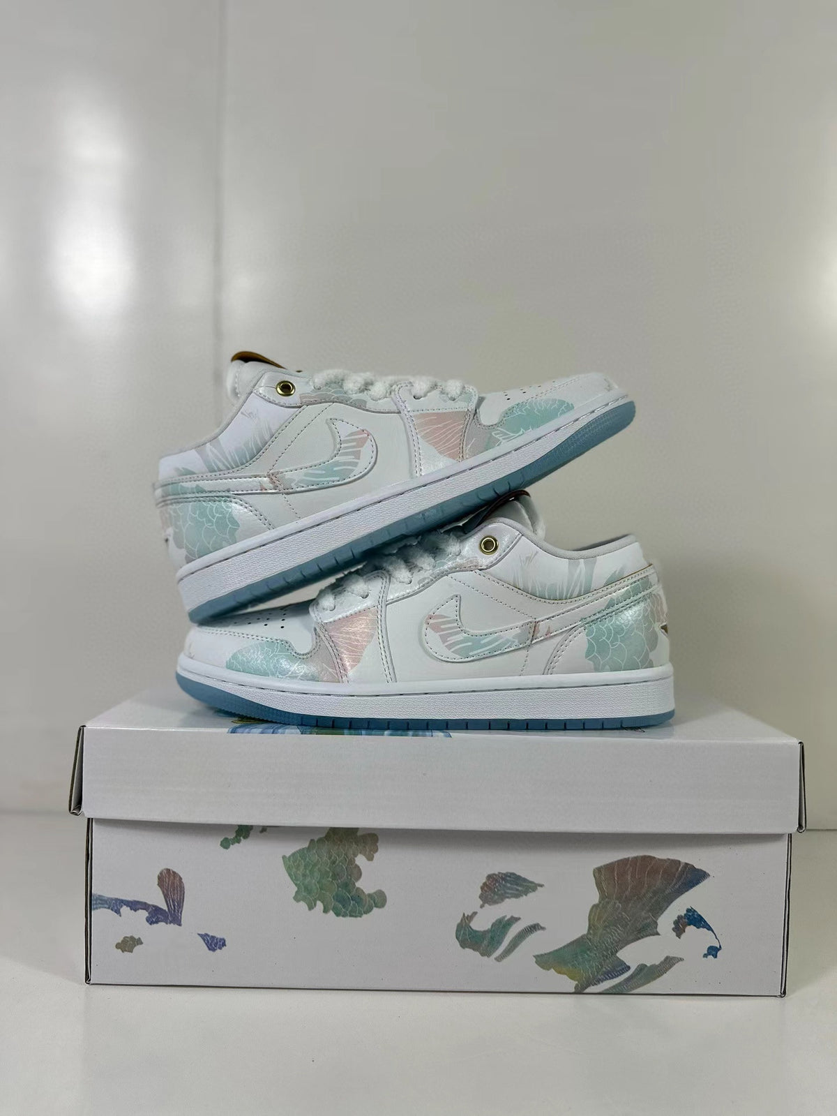 Pair of white low-top Jordan sneakers with pastel blue-green and pink accents displayed on an illustrated shoe box.