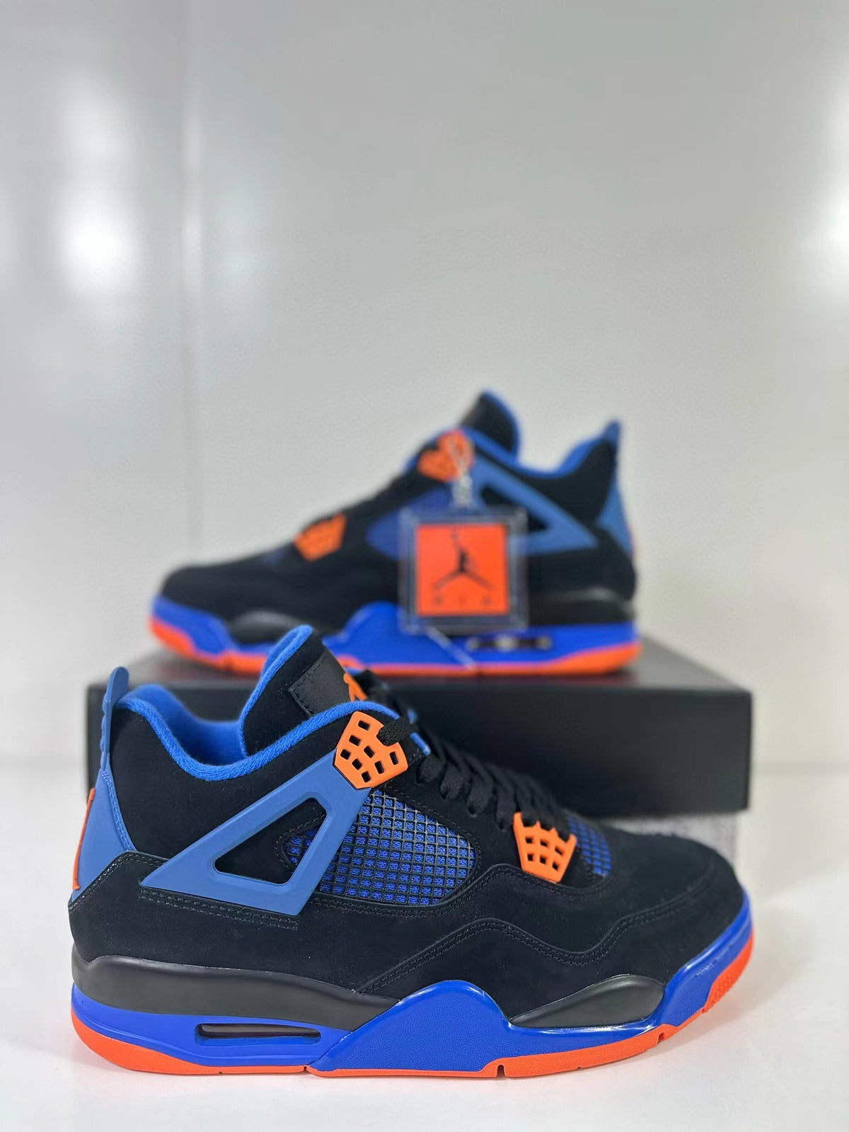 Close three-quarter view of the black, blue and orange Air Jordan 4 sneaker with attached hangtag.