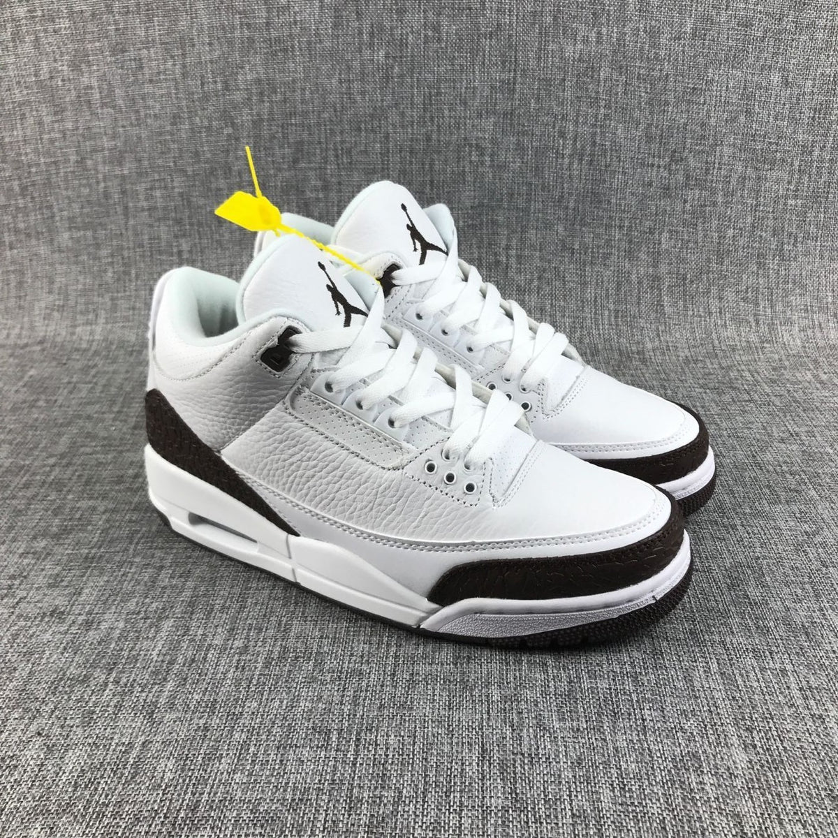 Three-quarter front view of the pair showing white laces, brown toe overlays, and black tongue logos.