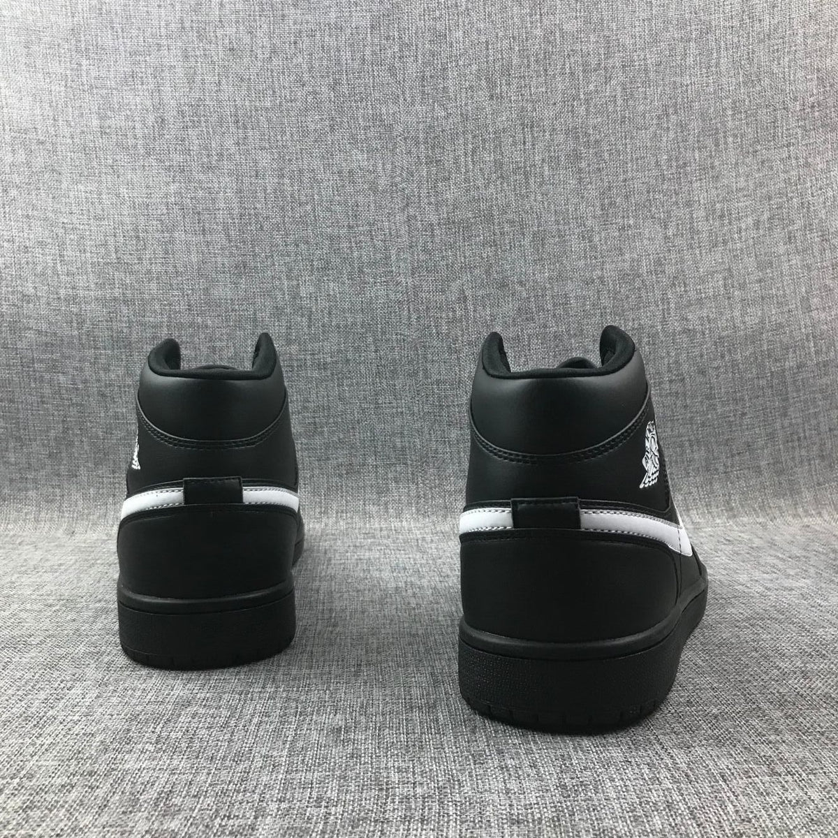 Rear view of a pair of black sneakers showing padded collars and contrasting white heel stripes.