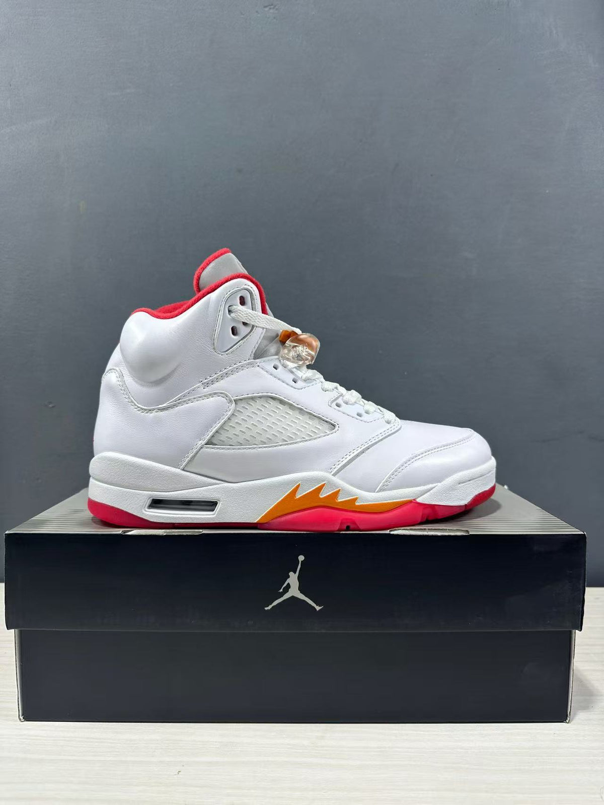 Side profile of a white Jordan high-top sneaker with a red collar, orange midsole accent and translucent side panel.