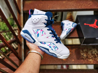 White Air Jordan 6 sneaker with blue and pink accents, multicolor patterned panels, and a Jordan shoebox in the background.