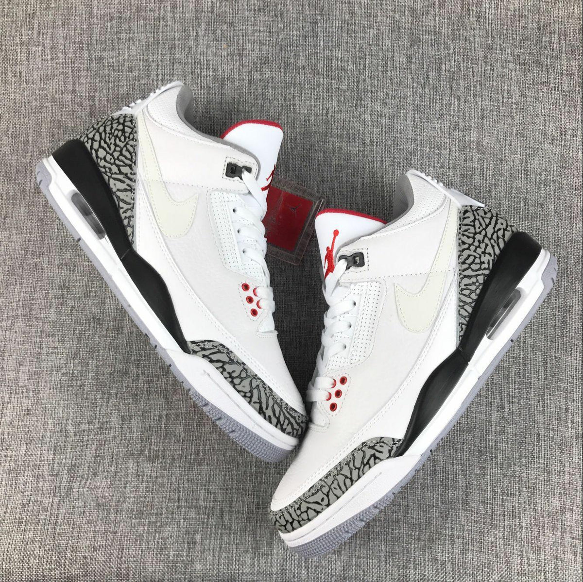 Top-down view of a pair of white Jordan sneakers with grey elephant-print overlays and red tongue accents.