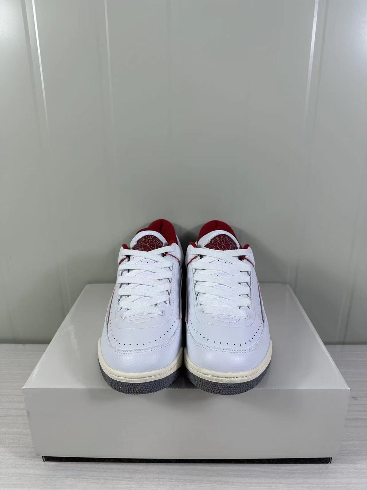 Front view of white and red low-top Jordan sneakers with perforated toe panels and white laces.