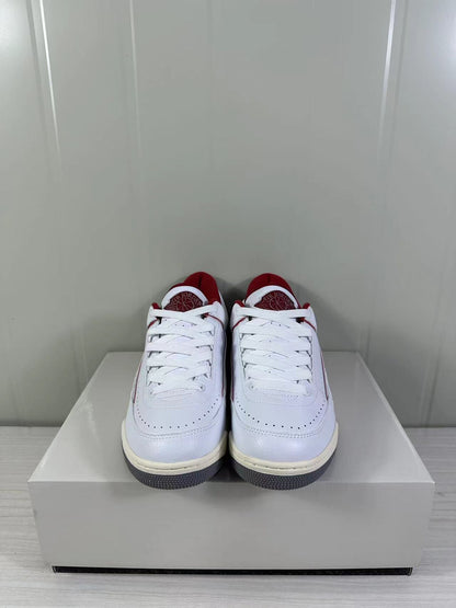 Front view of white and red low-top Jordan sneakers with perforated toe panels and white laces.