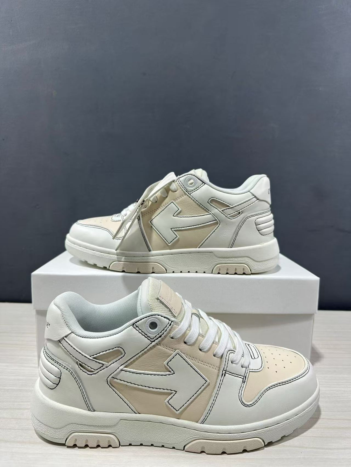 Two cream-white sneakers shown from side and three-quarter angles, highlighting layered panels and arrow motifs.