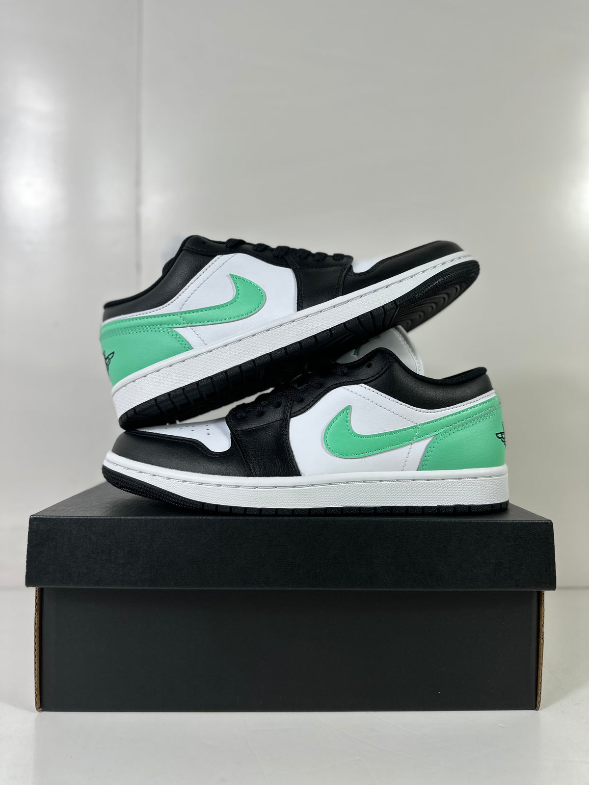 Pair of white, green, and black low-top sneakers arranged on a black shoebox.