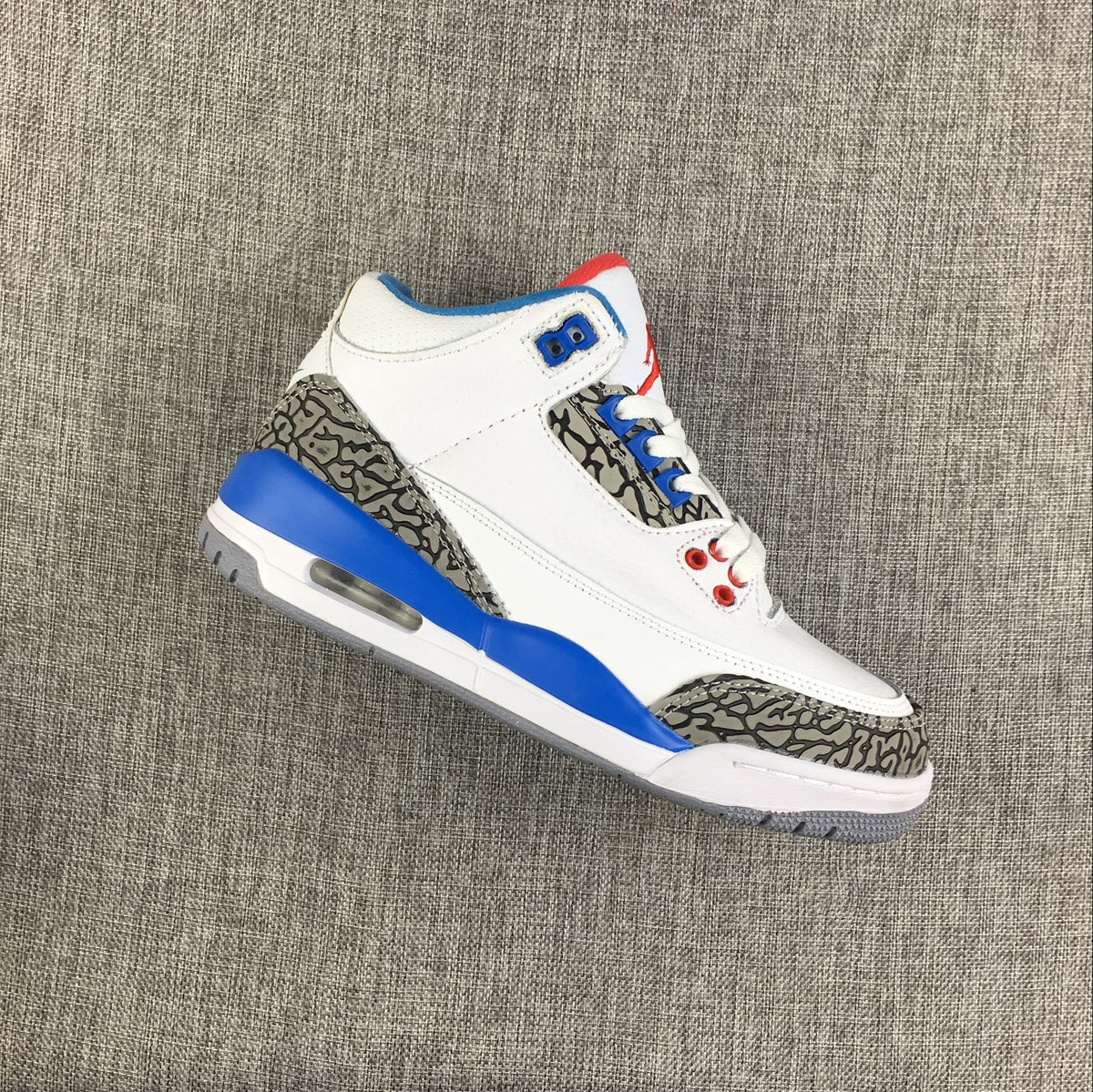 Angled view of a white Air Jordan 3 Retro sneaker showing elephant-print overlays and blue accents.