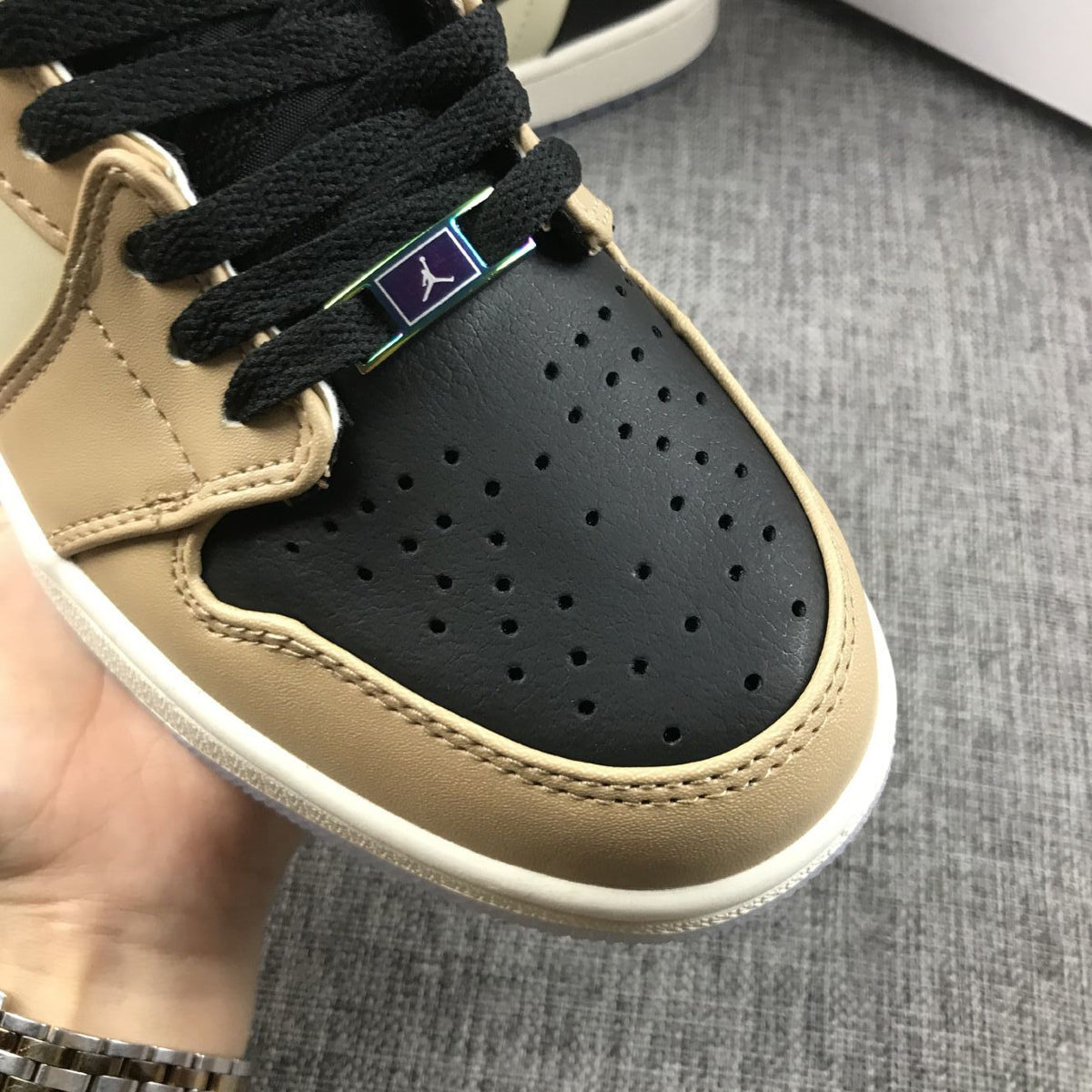 Close-up of a black perforated toe panel with black laces and a decorative lace tag.