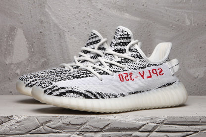 Pair of black-and-white knit sneakers shown from a three-quarter side angle with white laces and red side lettering.