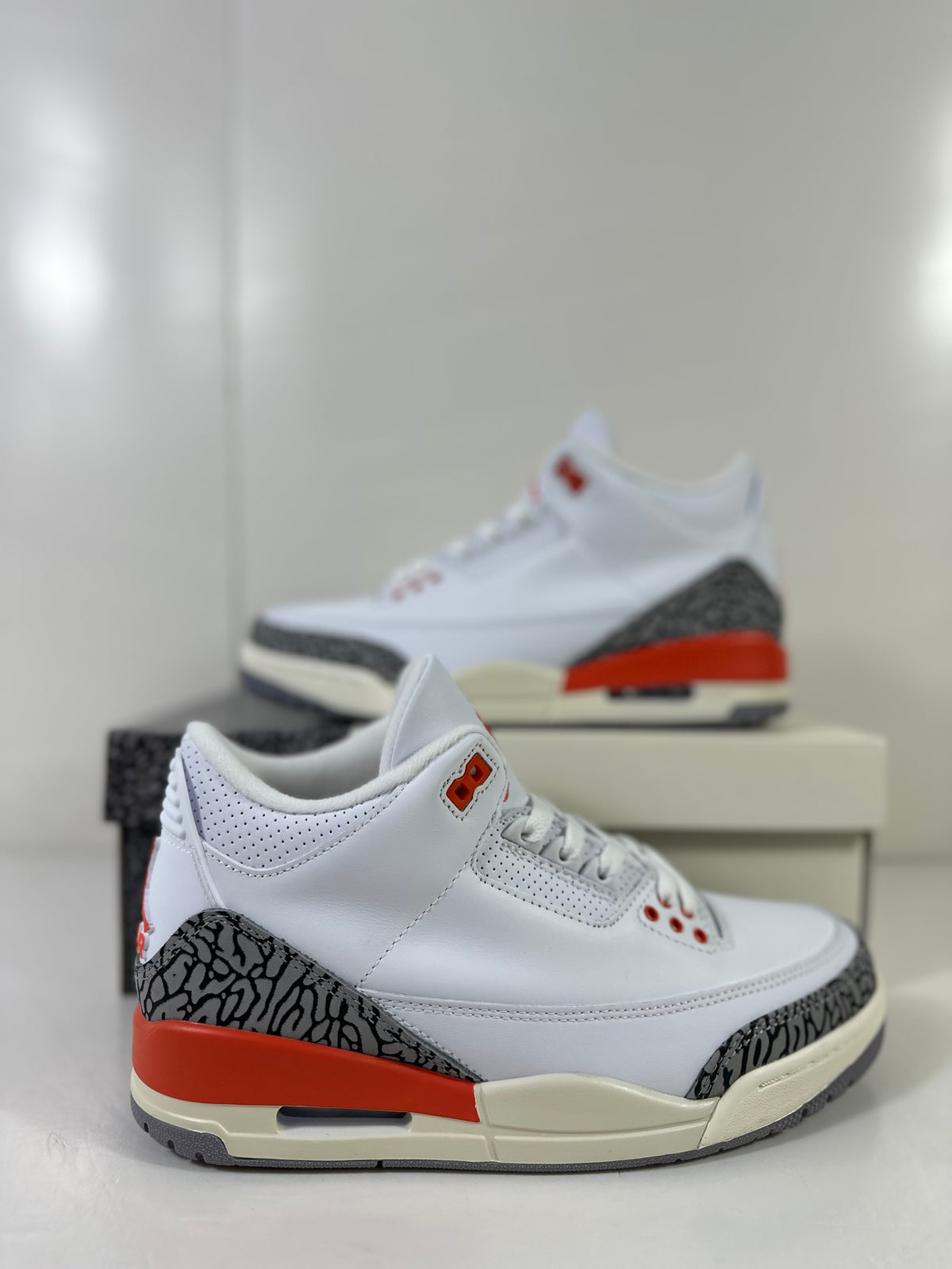 Close side view showing the white upper, grey elephant-print overlays, red heel accent, and perforated collar.